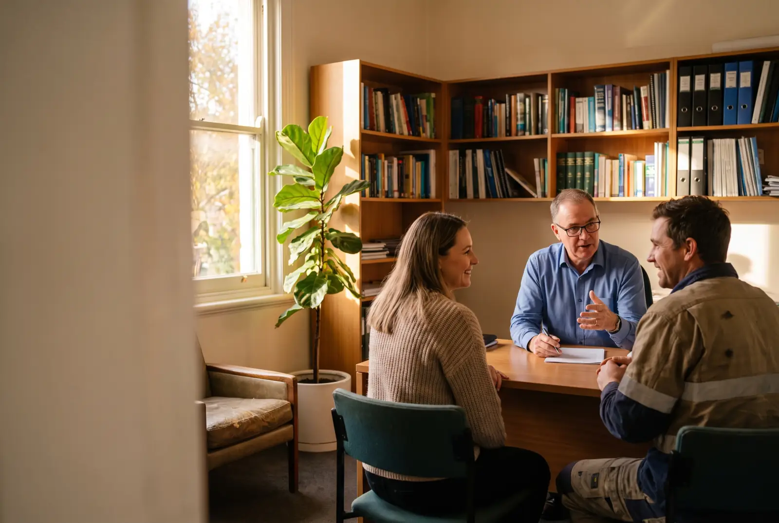 An accountant talks through paperwork with two small-business owners in an office lined with bookshelves